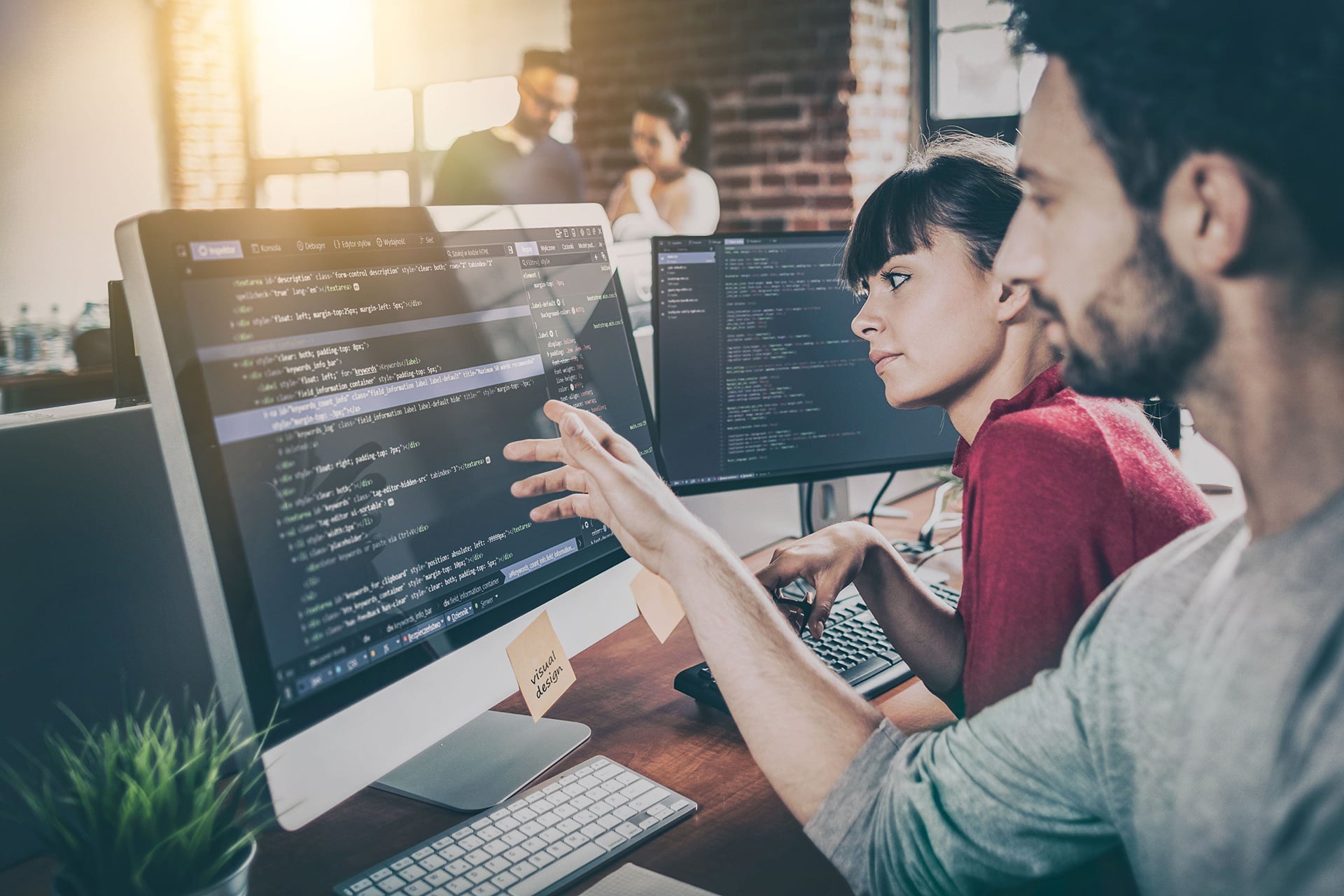 Two developers working on a monitor with code, analyzing and optimizing CI/CD test pipelines in a modern office.